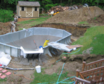 Pool walls are assembled and the walk-in pool step is secured in place using concrete. The pool bottom material has been put in place.