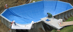 Final steps of the pool liner installation. The green vacuum sitting near the pool wall is used to vacuum air out from behind the liner, causing it to lay against the walls and the pool bottom.